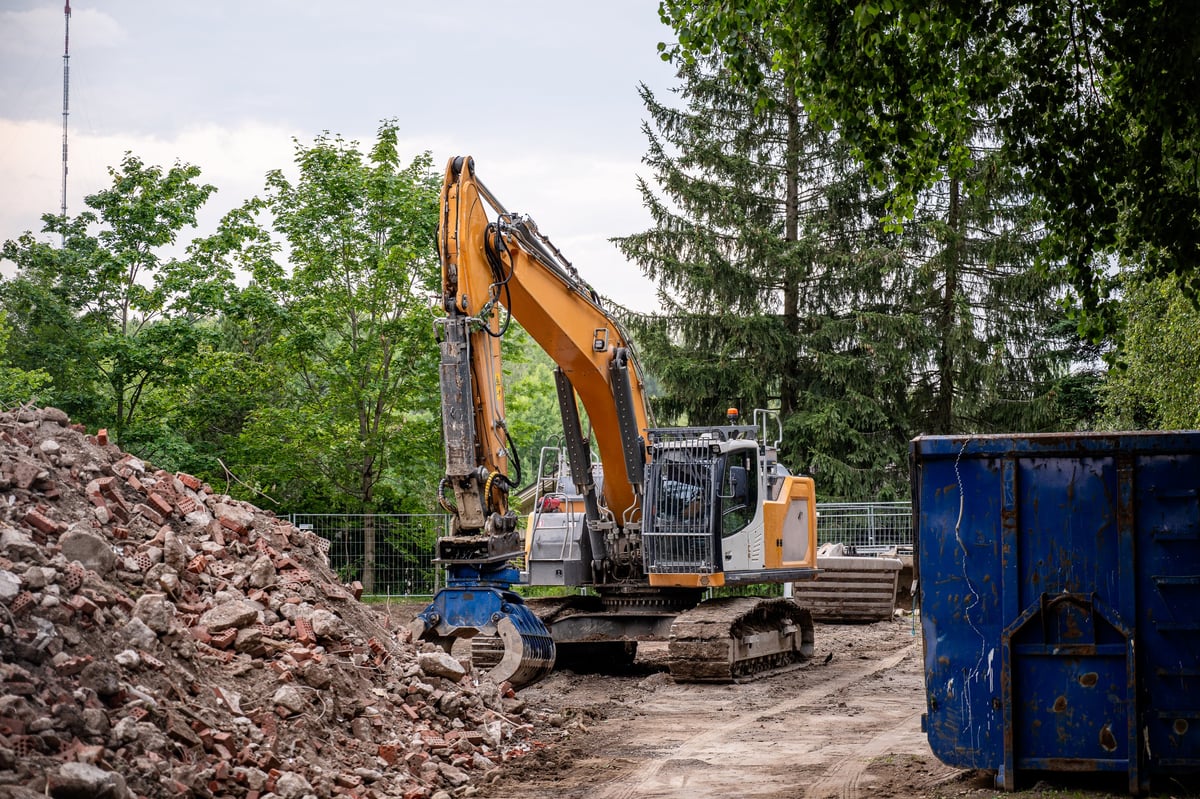 Tracked excavator working at a demolition site with rubble and a metal dumpster