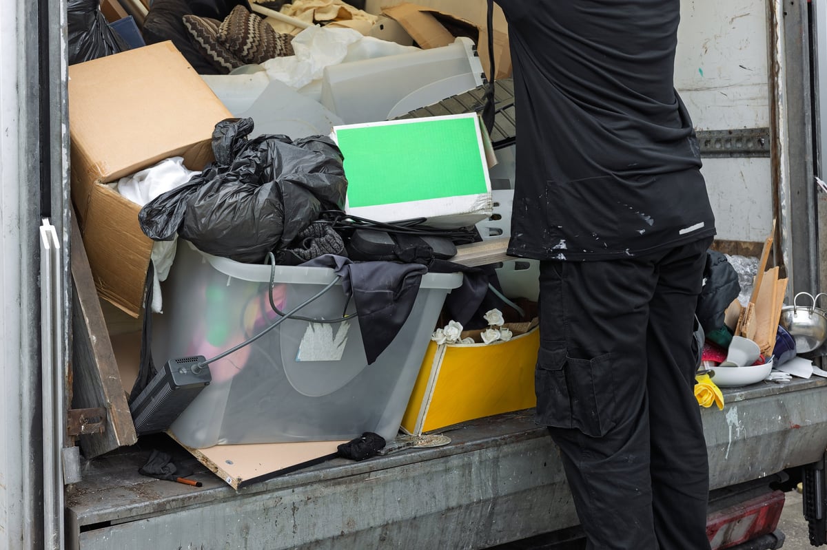 Worker unloading mixed waste and household items from the rear of a hauling truck