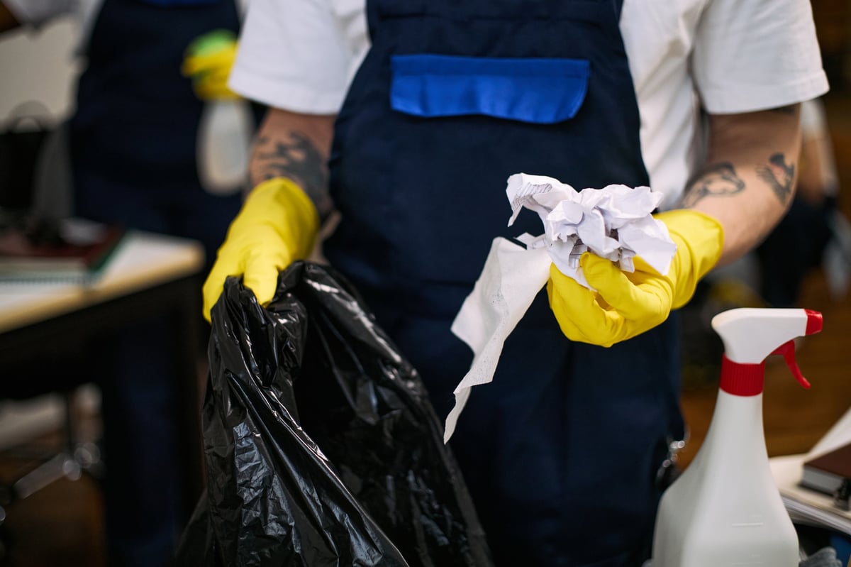 Man in yellow gloves clearing an office workspace into a garbage bag